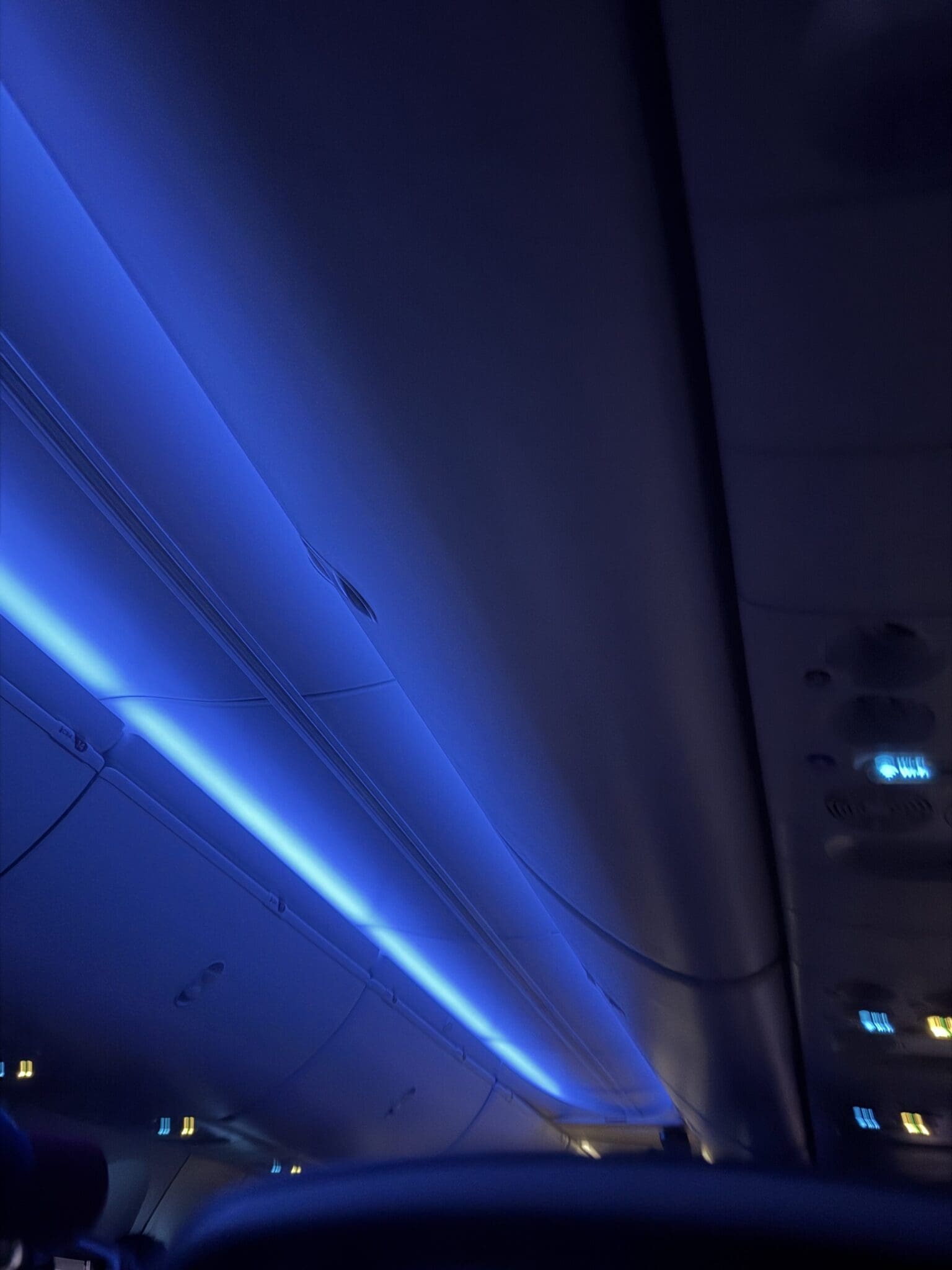 Airplane cabin interior illuminated by deep blue sleep-inducing LED lighting.