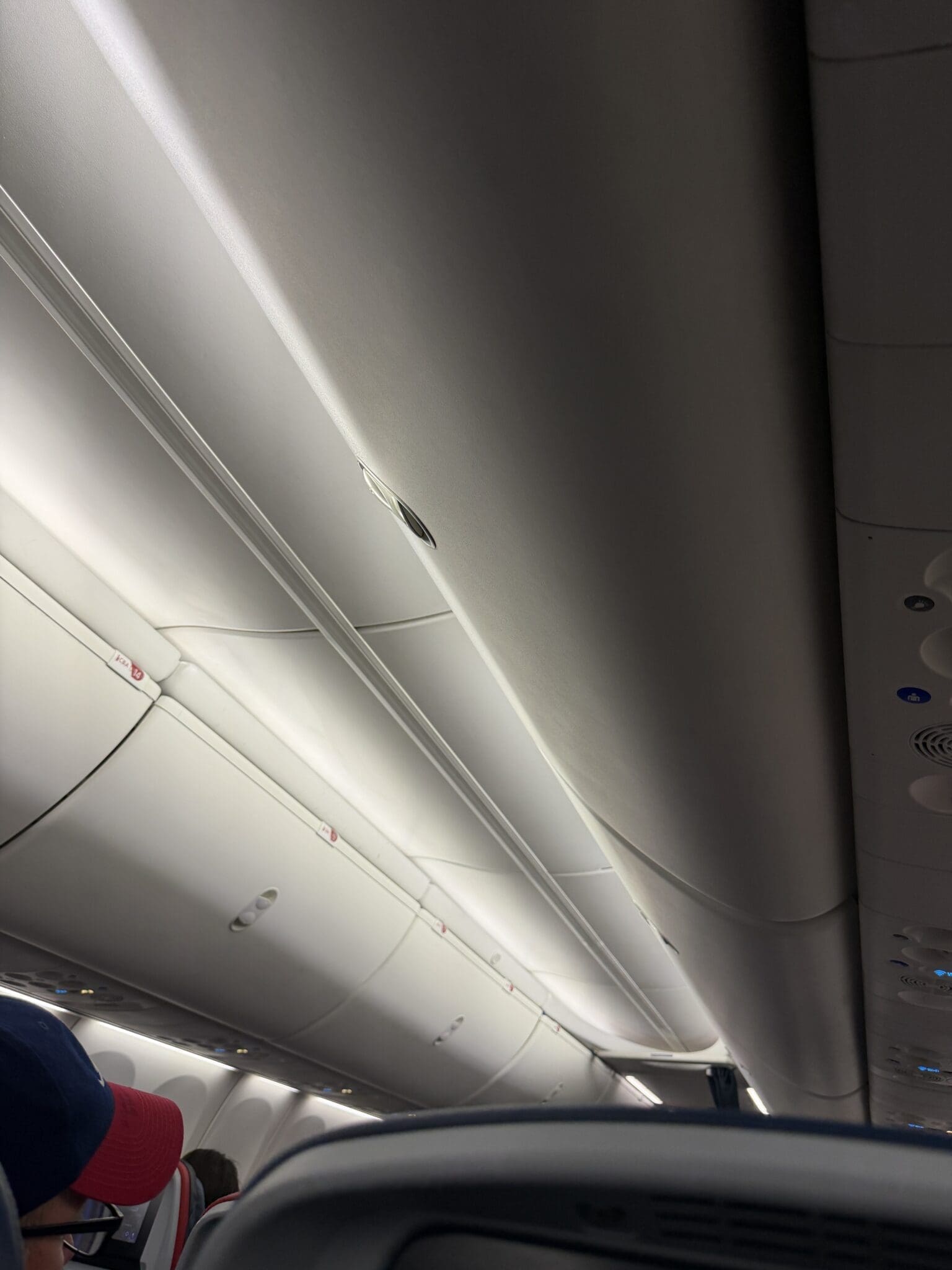 Airplane cabin interior harshly lit by bright white fluorescent lighting, disrupting sleep mid-flight.