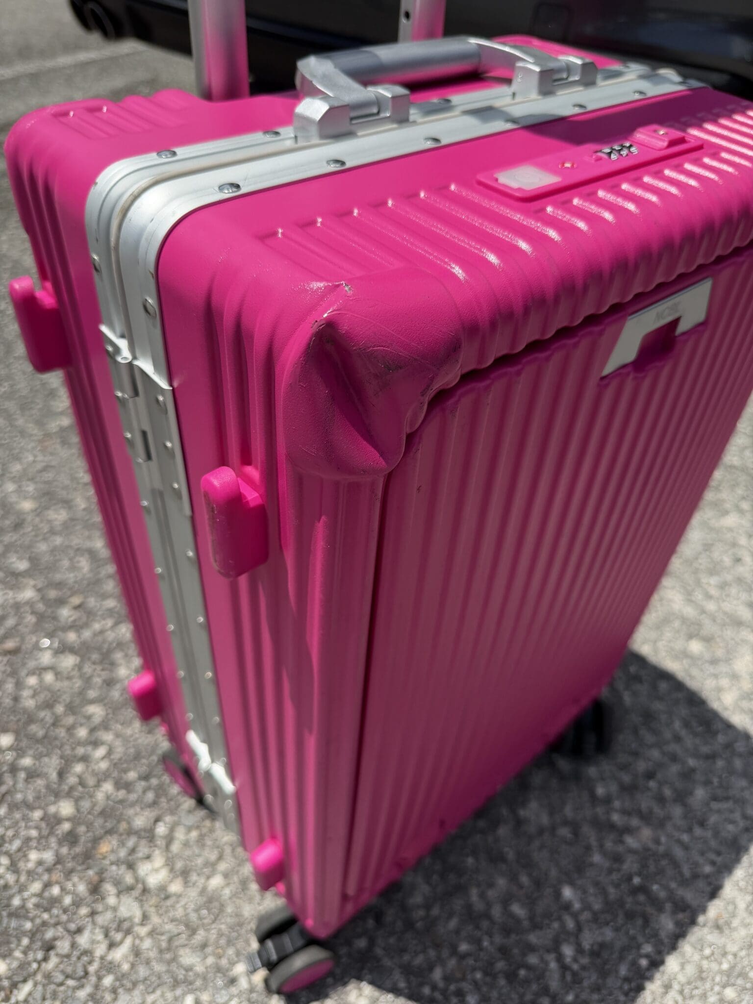 Pink NOBL suitcase showing a severely dented corner after being gate-checked at the airport
