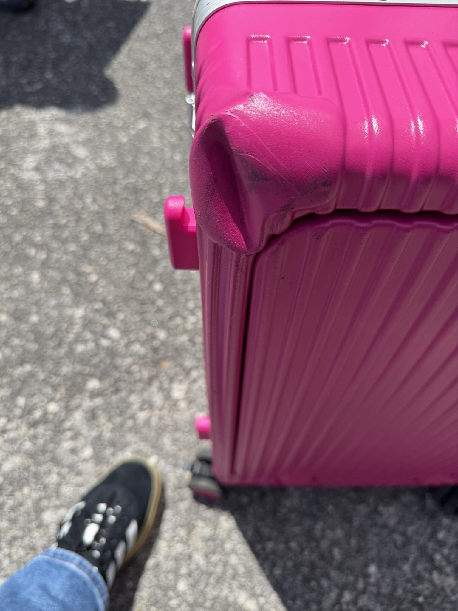 Close up of a bright pink NOBL carry-on suitcase with a deeply crushed and scuffed top corner